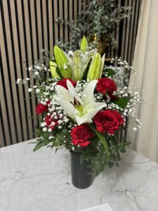 Arreglo delante del mostrador de la floristería San Ildefonso con claveles rojos y lírios blancos