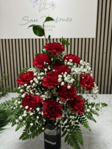 Arreglo delante del mostrador de la floristería San Ildefonso con claveles rojos de cerca